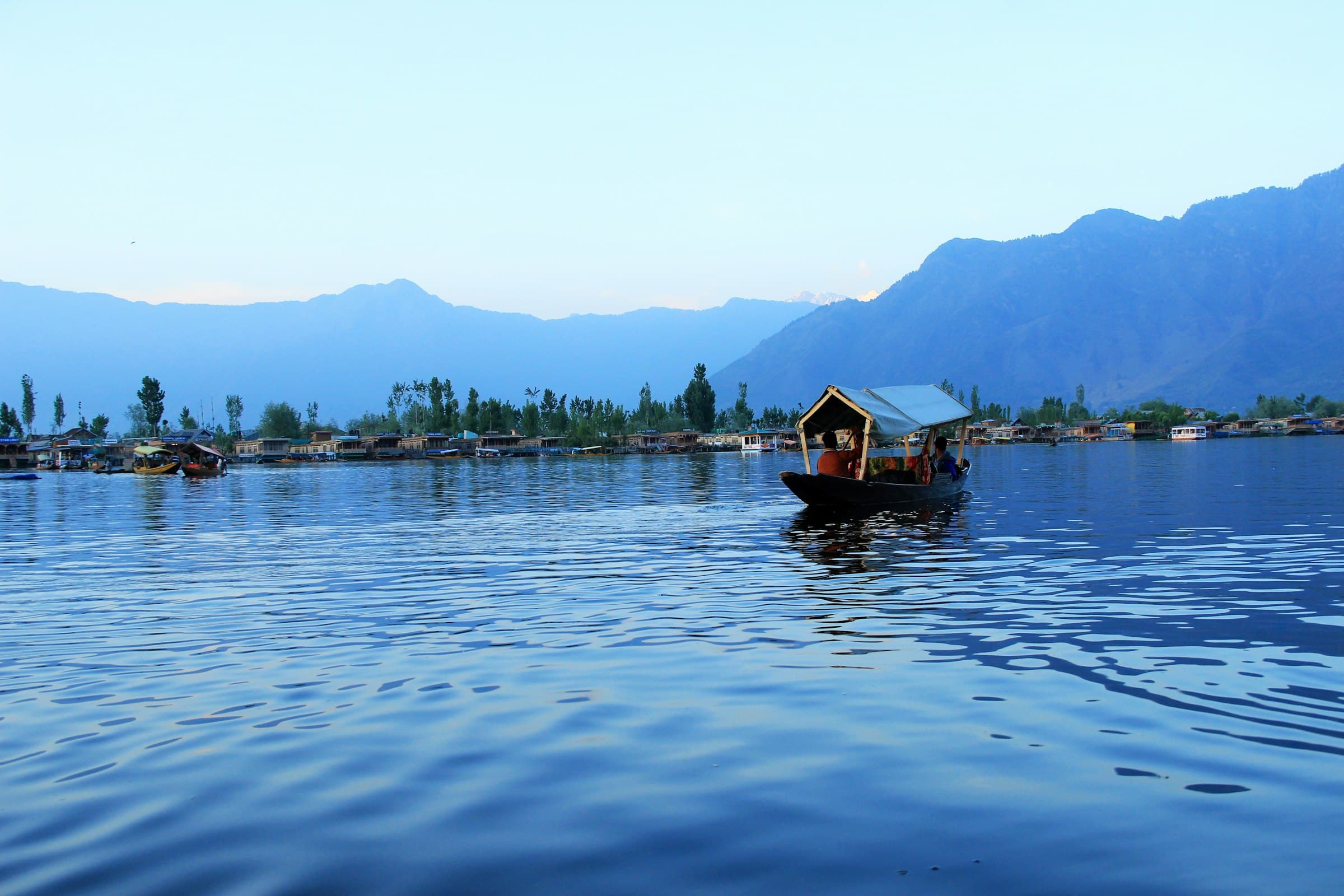 A shikara crossing Dal Lake in Srinagar beneath blue mountains
