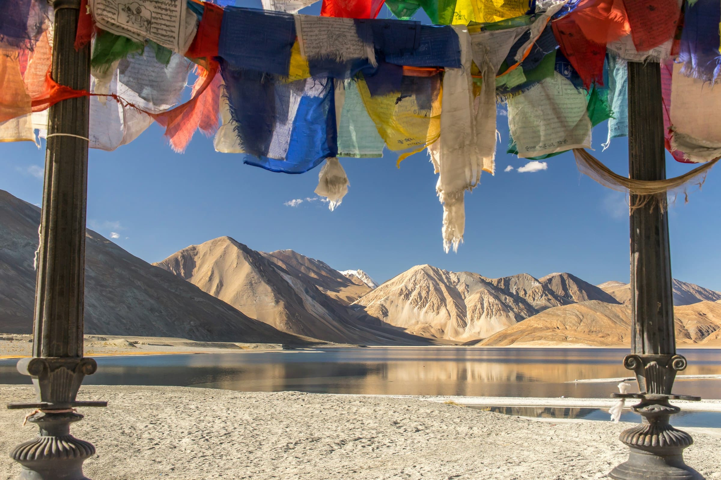 Prayer flags framing Pangong Lake and the mountains of Ladakh