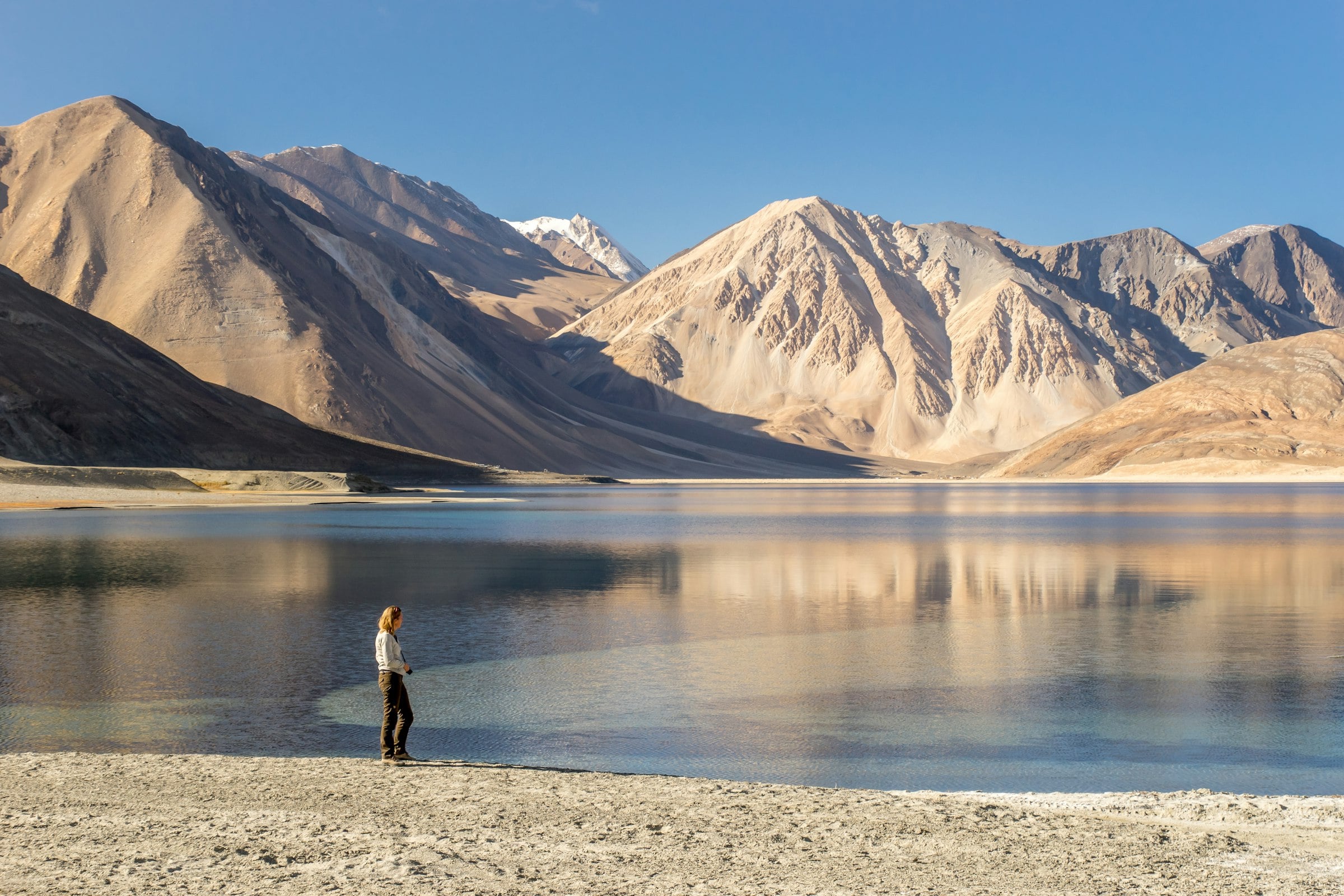 A traveller on the shore of Pangong Lake beneath bare mountains
