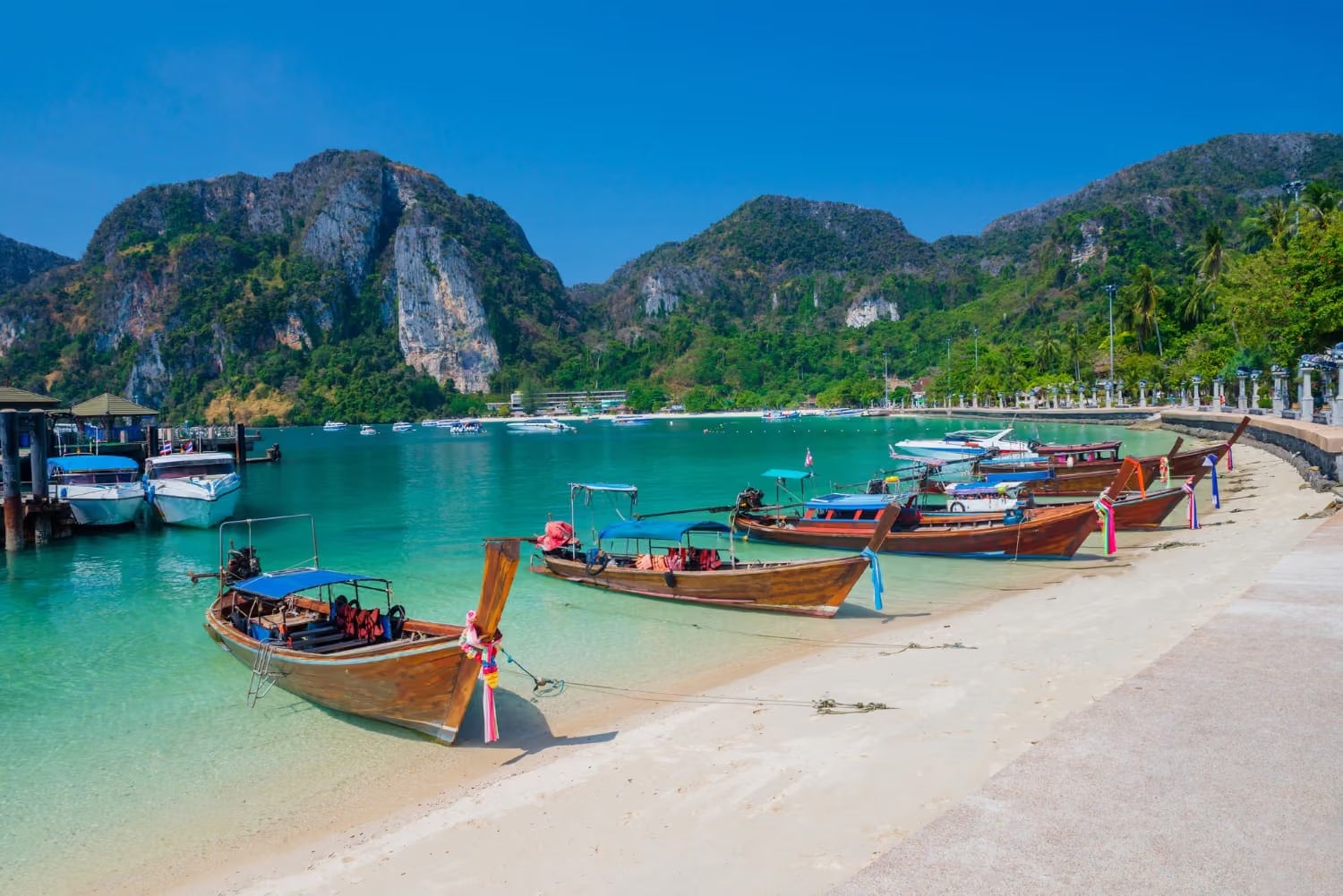 Longtail boats moored along a white-sand beach in the Phi Phi Islands