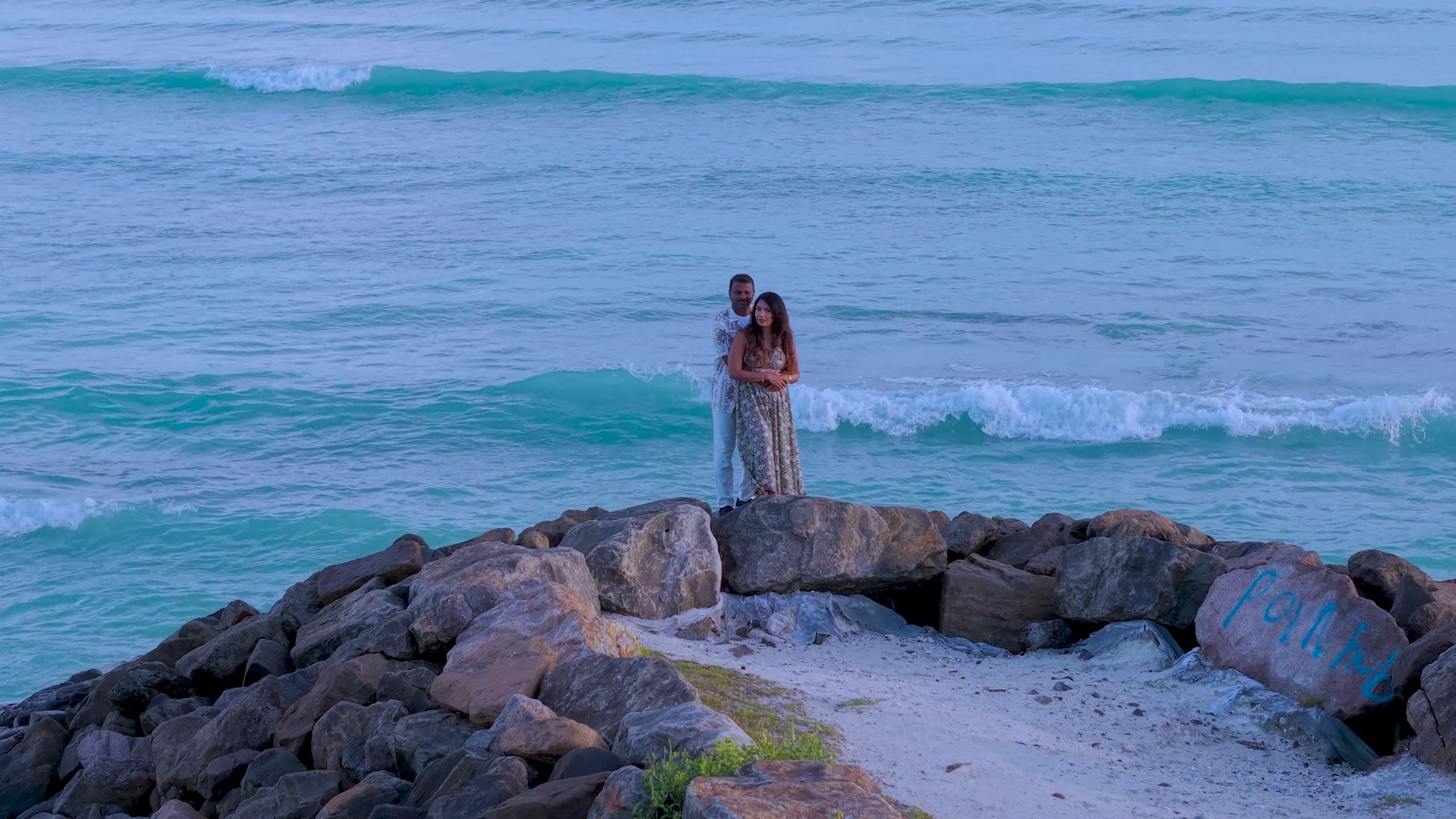 A couple on a rocky point above the sea at dusk