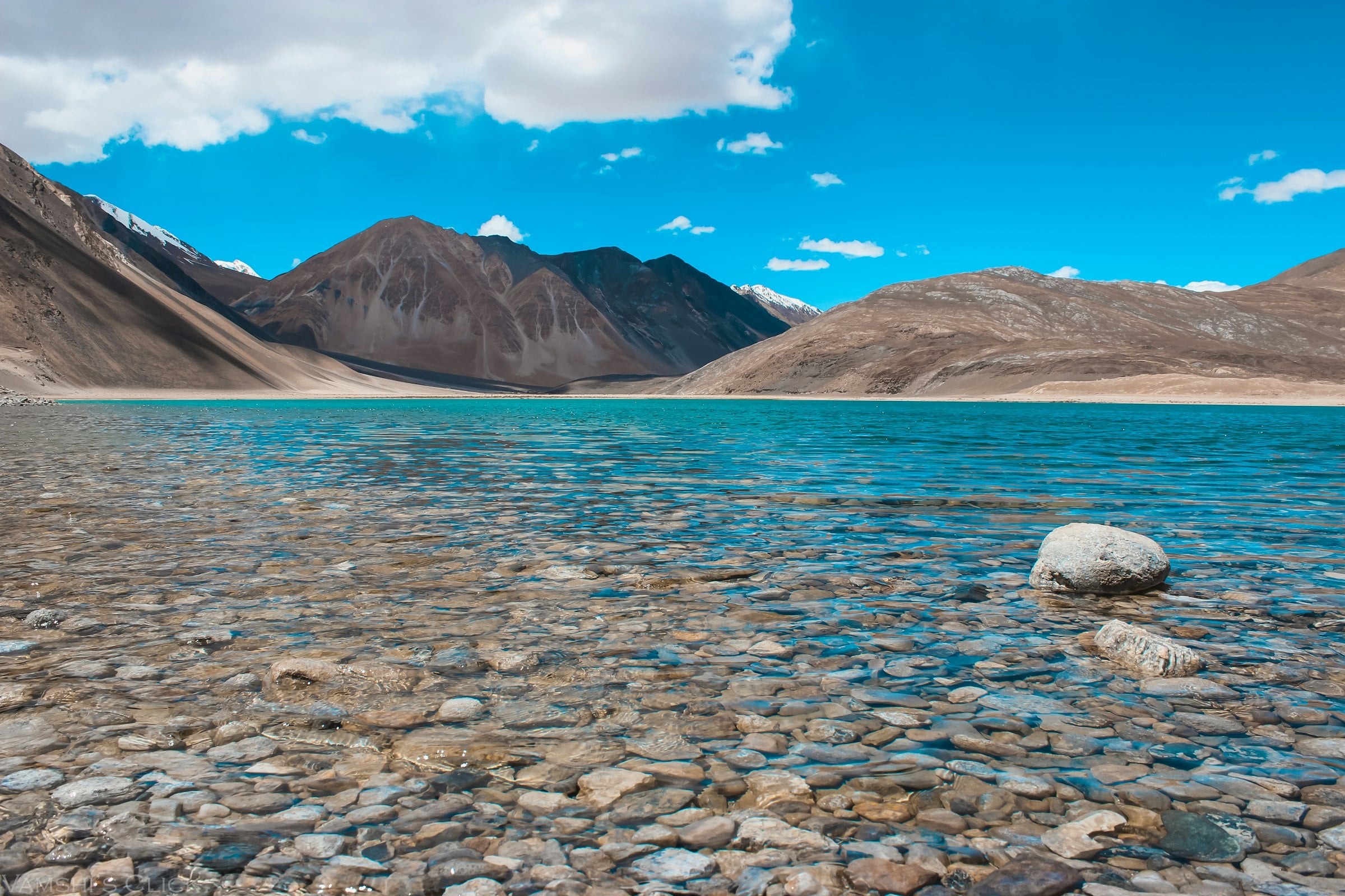 Clear water over the stones of Pangong Lake, beneath the mountains of Ladakh